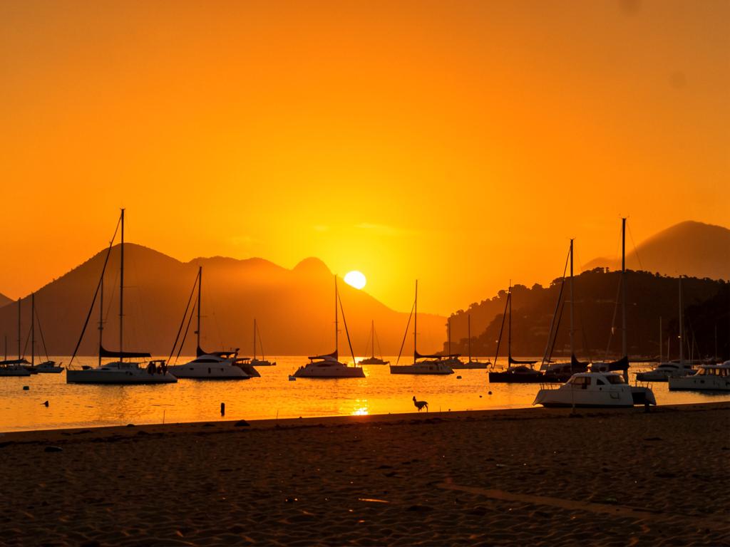 Sol dourado se pondo no rio com barcos silhuetados